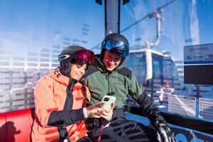 Zwei Skifahrer in einer Gondel schauen gemeinsam auf ein Handy. | © mr-offenblende.at