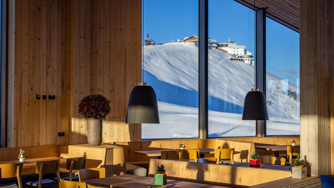 Interior view of the mountain restaurant Das Panorama with a snowy mountain backdrop. | © Nikolaus Faistauer Photography
