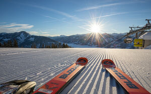 Ski und Sonnenaufgang auf einer weißen, präparierten Piste. | © Schmittenhöhebahn AG/Nikolaus Faistauer Photography