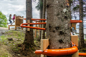 Kinder erkunden ein Spielgerät mit orangefarbenen Rohren im Wald. | © Gerald Lobenwein