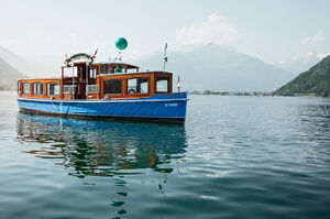 Das Dampfschiff Libelle schwimmt auf ruhigem Wasser mit Bergen im Hintergrund. | © Schmittenhöhebahn AG/Johannes Felsch 