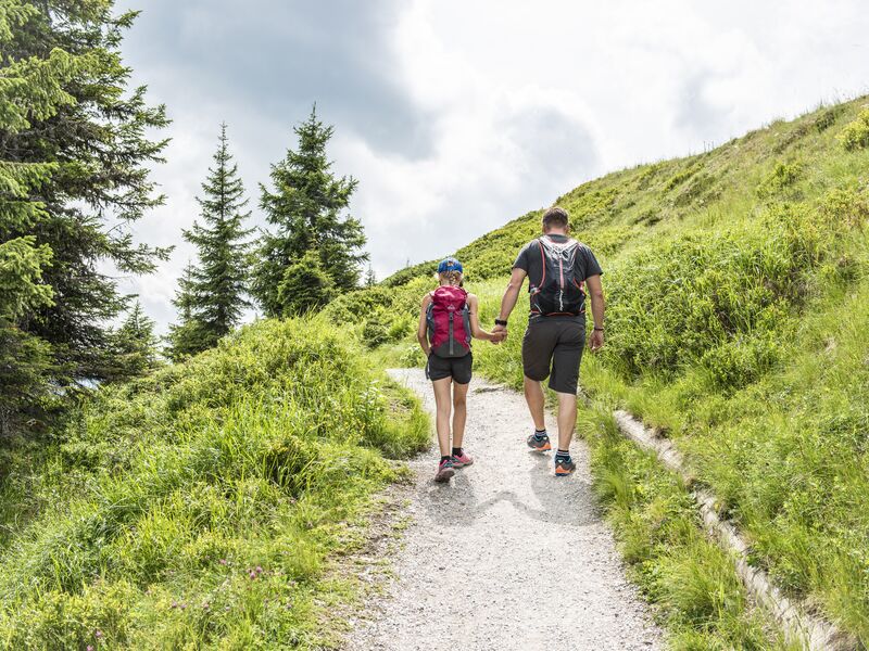 Zwei Personen gehen Hand in Hand einen Wanderweg entlang. | © Schmittenhöhebahn AG / Max Steinbauer