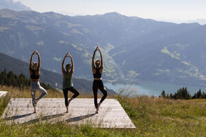 Drei Personen machen Yoga auf einer Plattform mit Bergblick über den Zeller See. | © kuscheiart