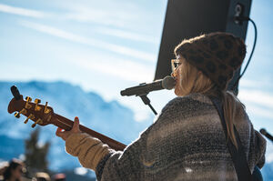 Frau mit Gitarre und Mikrofon, im Hintergrund ein Berg.