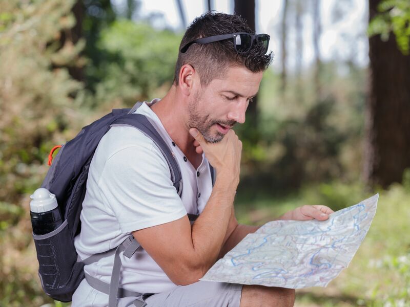 Ein Mann mit Rucksack betrachtet im Wald eine Karte. | © Phovoir