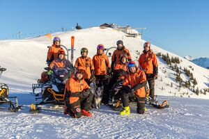 Gruppe in oranger Ausrüstung mit Schneemobil im Schnee. | © Nikolaus Faistauer Photography