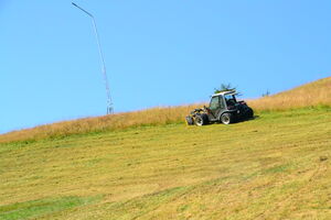 Ein Fahrzeug mäht Gras auf einer schrägen Wiese bei klarem Himmel. | © Schmittenhöhebahn AG
