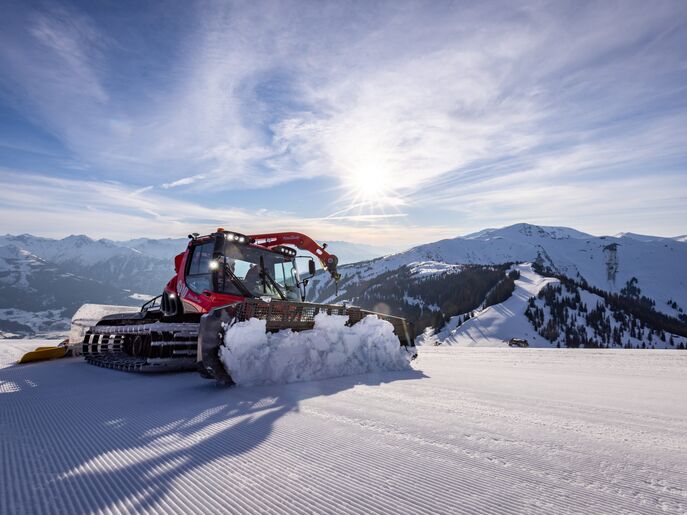 A snow groomer preparing a ski slope under sunny mountain skies. | © Nikolaus Faistauer Photography